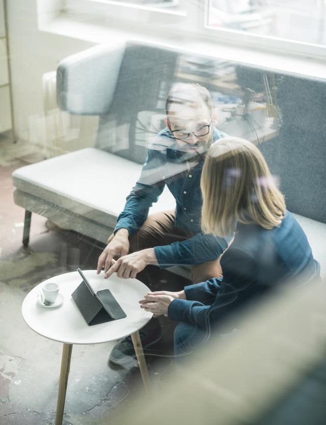 male and female sitting down and talking with tablet on table in front of them