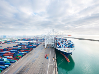 Vista di un porto commerciale con container di merci impilati e una nave attraccata carica di container