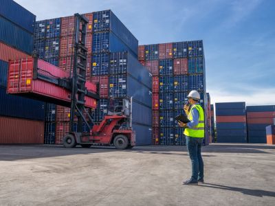 Un ingegnere dirige le operazioni logistiche in un deposito di container, indossando un casco di sicurezza e un giubbotto riflettente