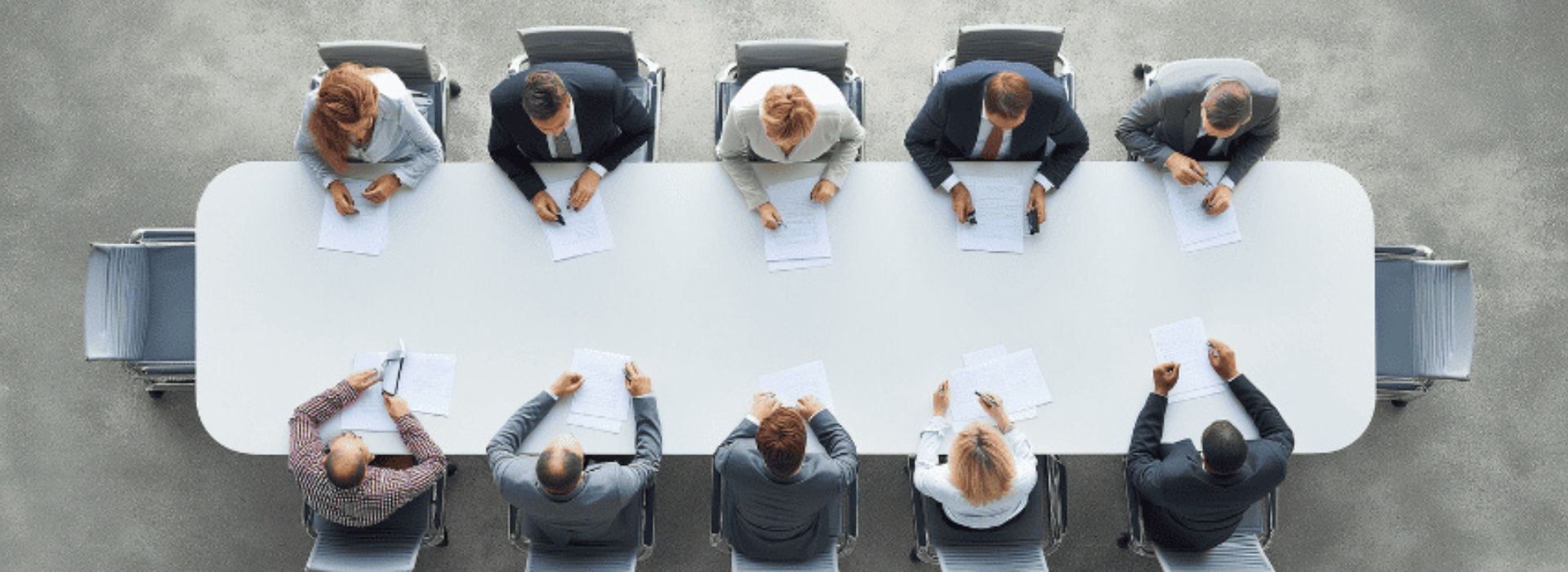Ripresa dall'alto di un business panel collaborativo durante un meeting raccolto intorno a un grande tavolo, per discutere strategie e idee