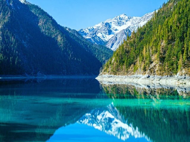 Panorama naturale con lago alpino circondato da montagne e foreste, simbolo di sostenibilità e rispetto per l’ambiente.