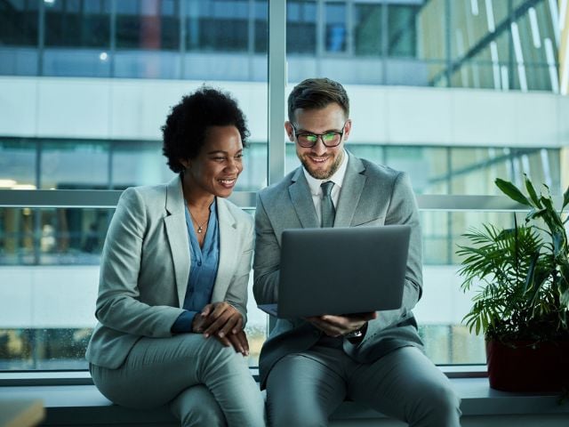 Due persone che guardano lo schemo del computer e sorridono