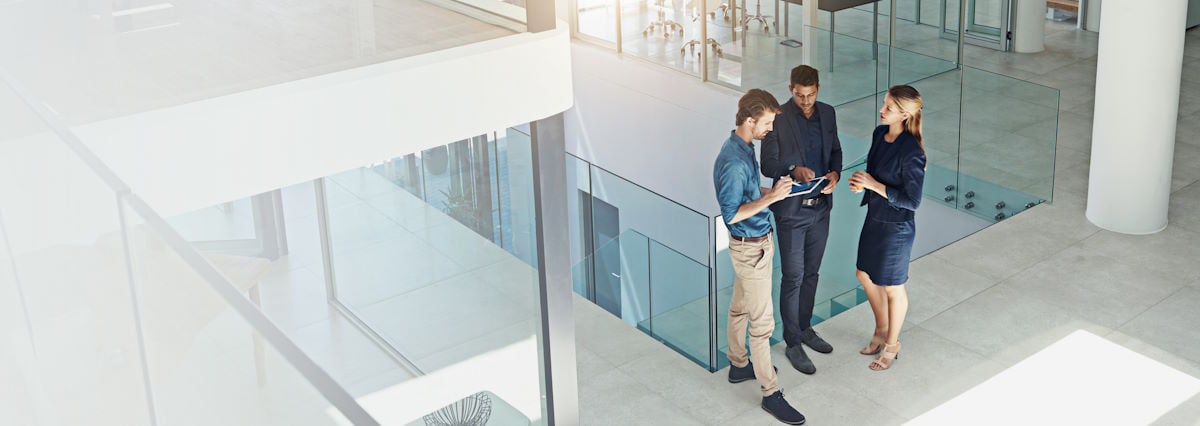 3 business people standing up and talking in a glass office