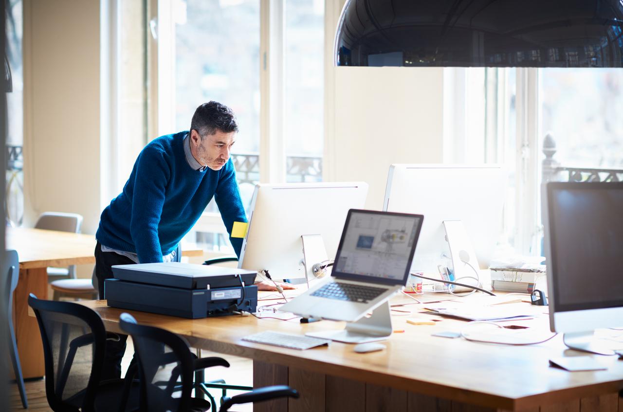 man leaning forward while standing up and looking computer