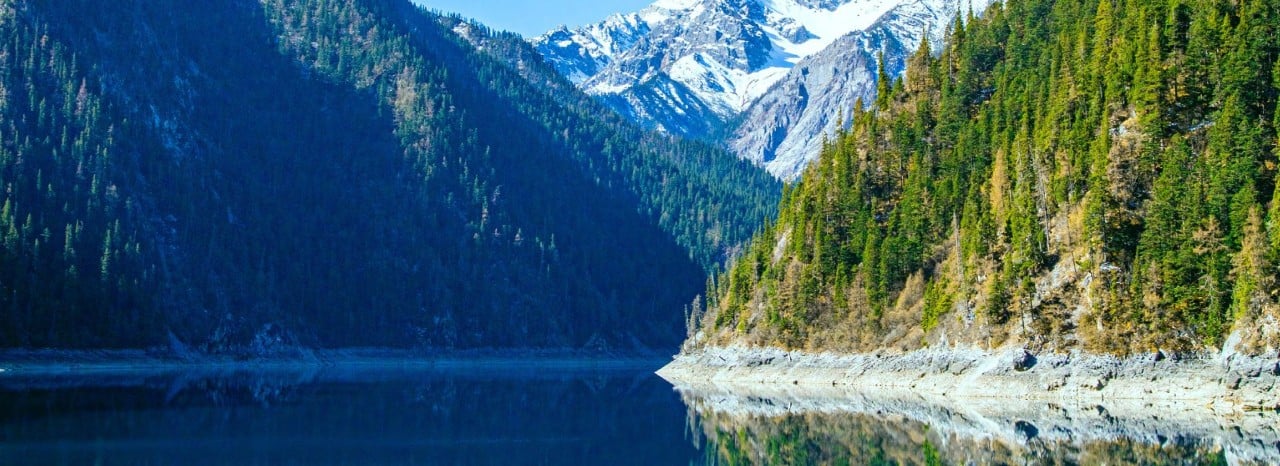 Panorama naturale con lago alpino circondato da montagne e foreste, simbolo di sostenibilità e rispetto per l’ambiente.