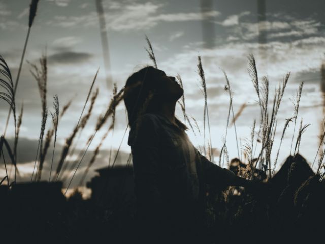 Giovane ragazza in un campo con il viso rivolto verso il cielo nuvoloso.