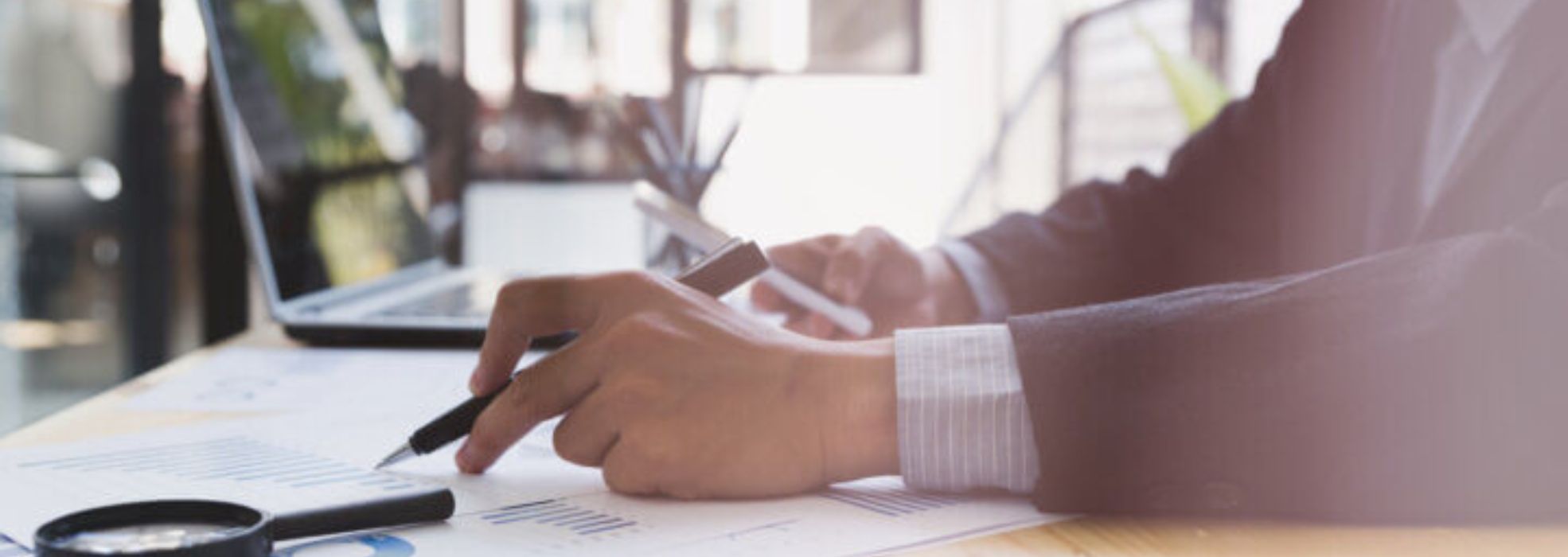 Man in business atire with pen in one hand and mobile phone in the otherhand. He is at desk working and analyzing business matters 