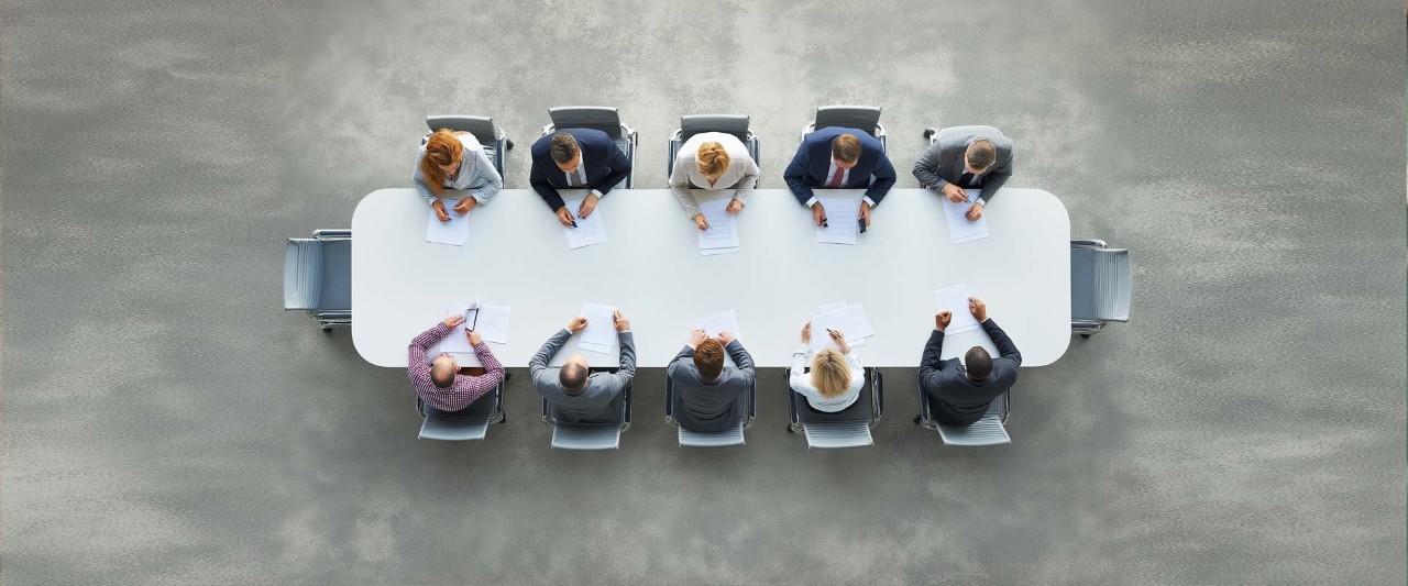 Overhead top view of a business panel collaborating during an office meeting, gathered around a large table to discuss strategies and ideas