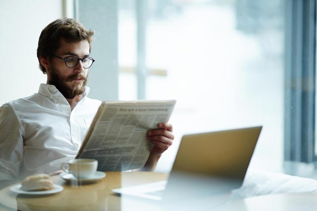 Man in fornt of laptop with the newspaper
