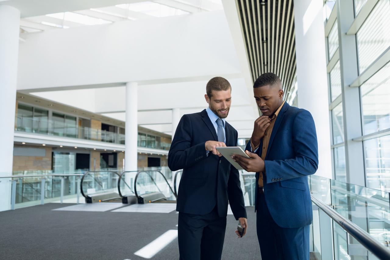 Two men in suits are discussing business matters over a tablet.