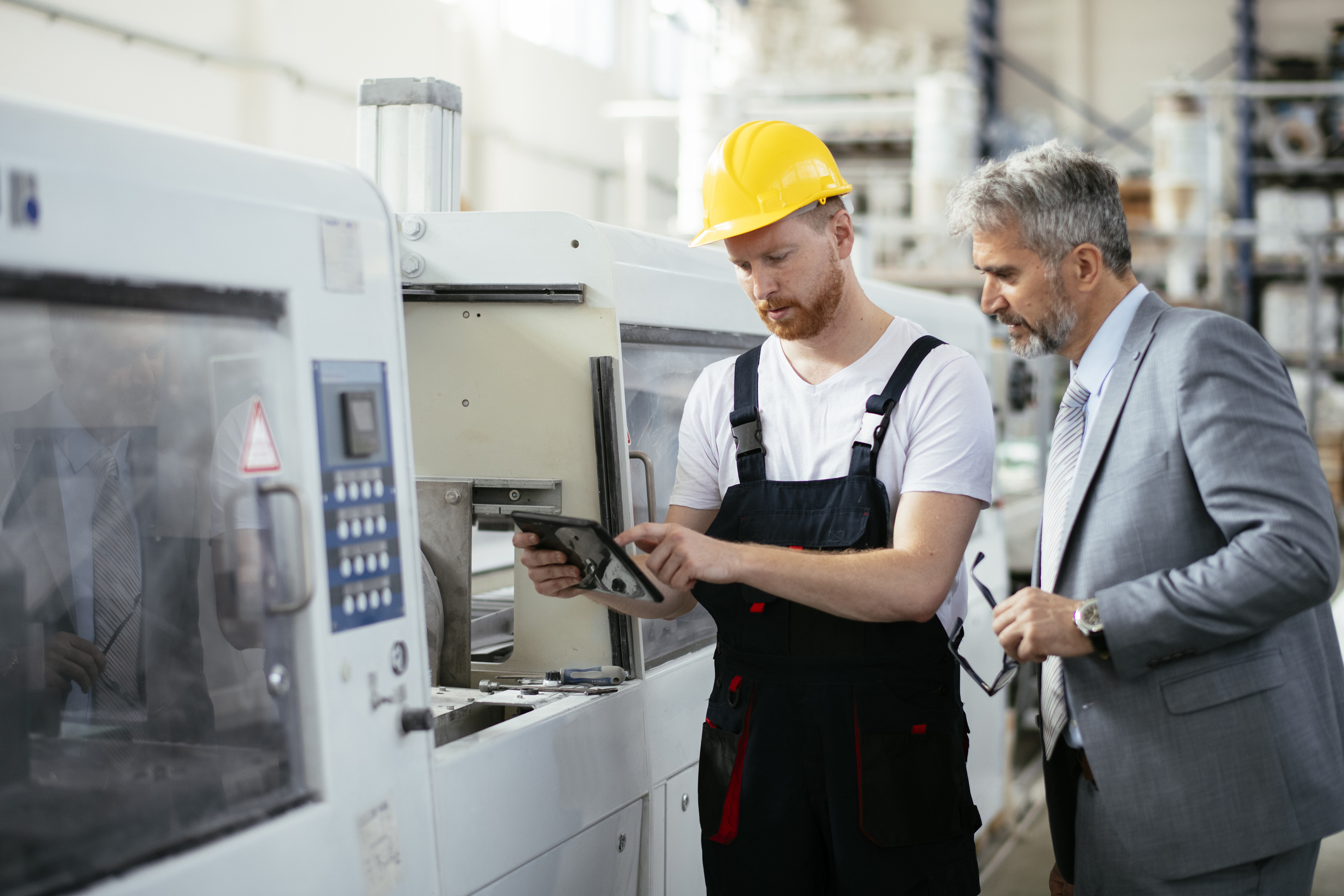 man with hard hat on showing another man wearing a suit a tablet