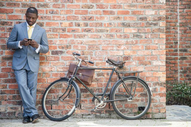 African-American male looking at cell phone while standing next to a bike