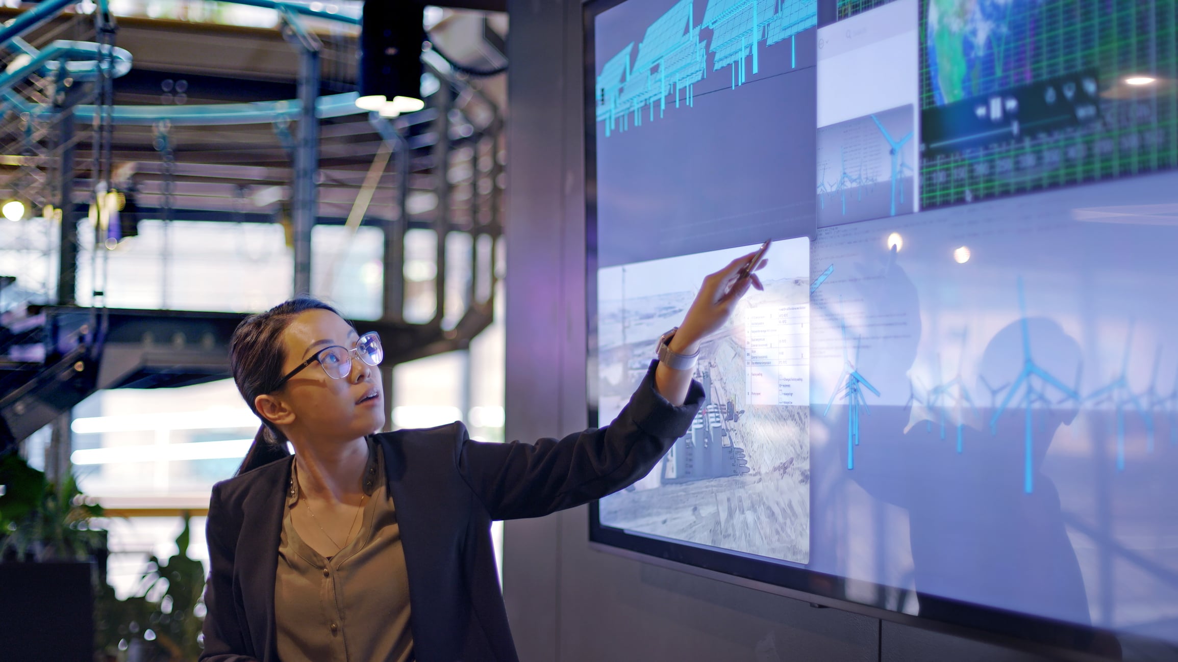 woman with glasses pointing at large screen