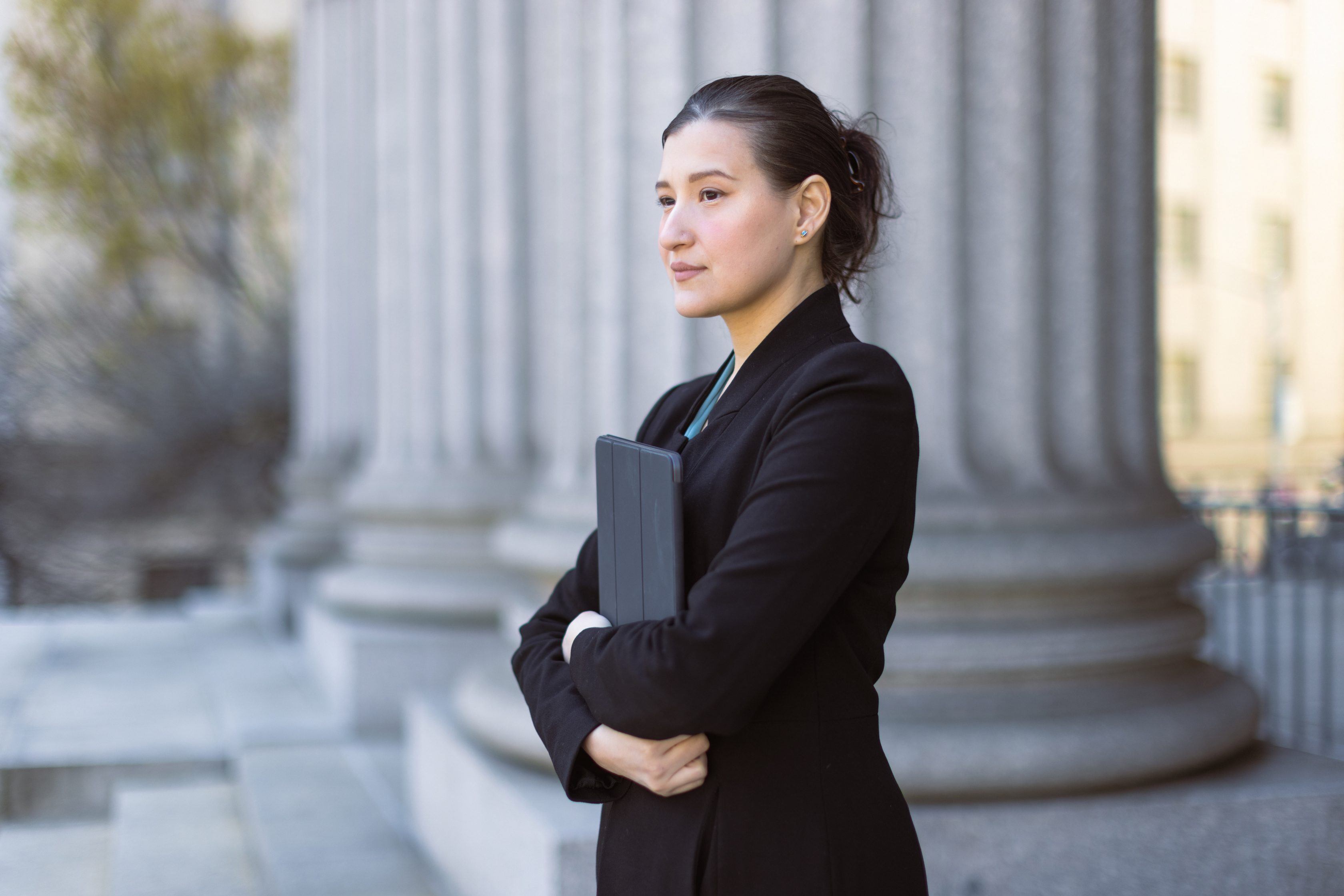 woman standing stoicly with arms crossed with folder in between them
