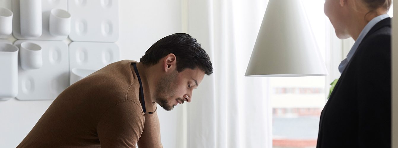 man in office writing down on paper while standing up as a colleague walks by