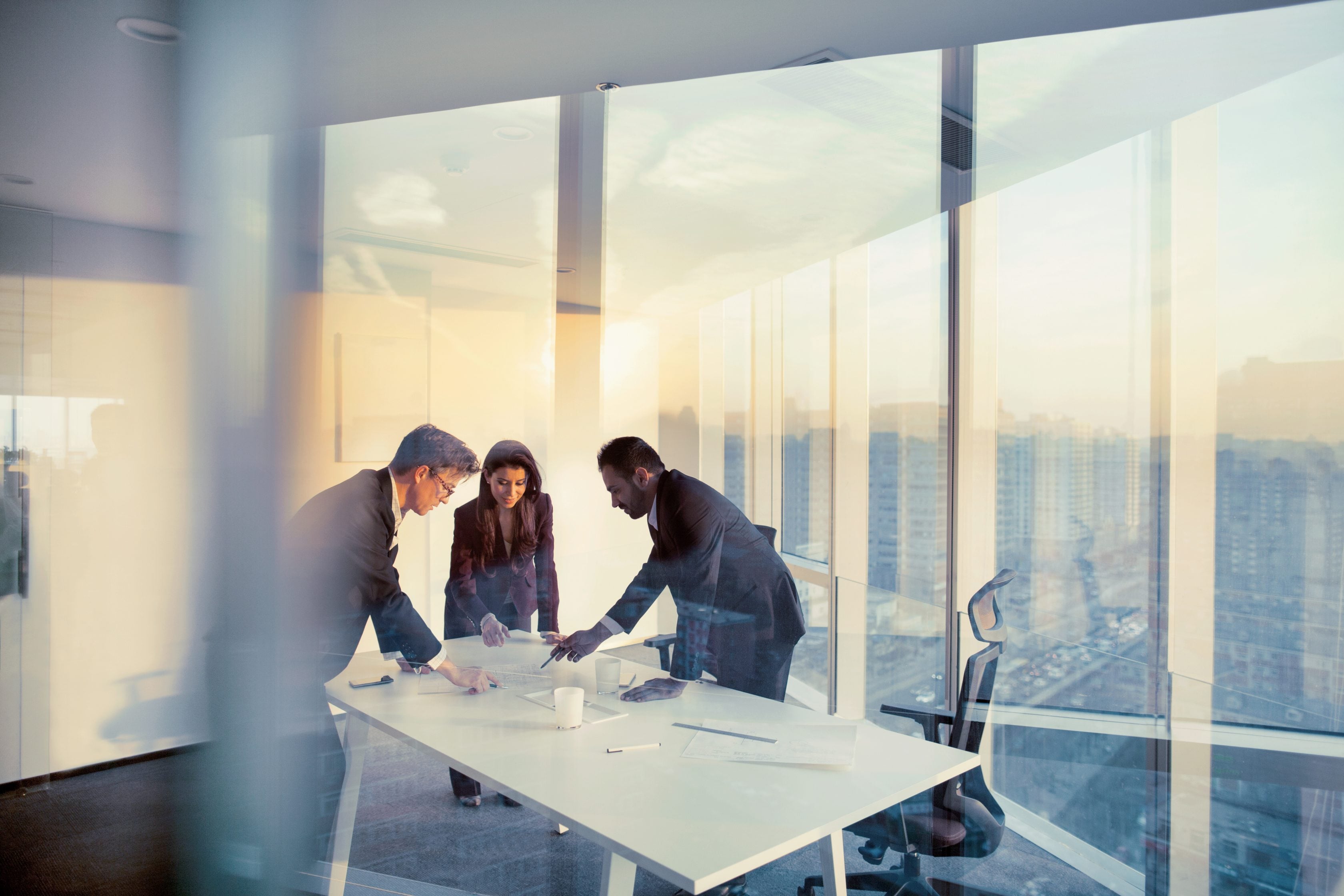 group of co workers in office room looking down at documents on a table