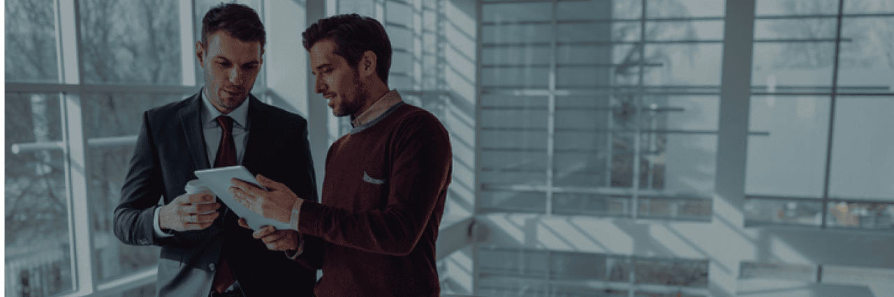 two men in a building, looking at something on a tablet