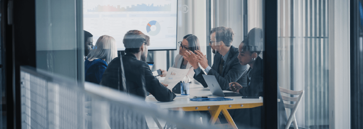 Business Leaders Sit Around a Conference Table Reviewing Charts on a Large Screen