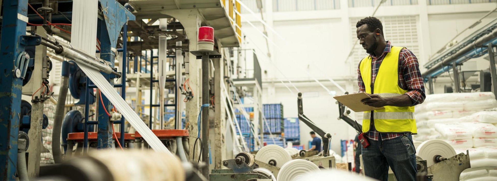Un tecnico con gilet giallo controlla il funzionamento dei macchinari in un'industria cartaria