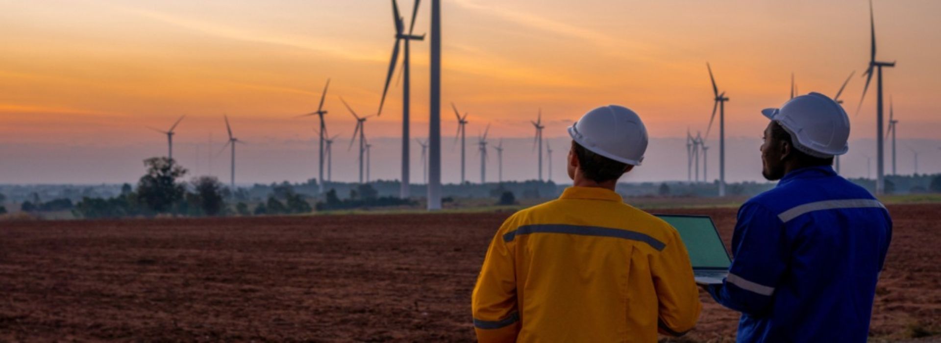 Due operai con casco protettivo lavorano in un parco eolico al tramonto