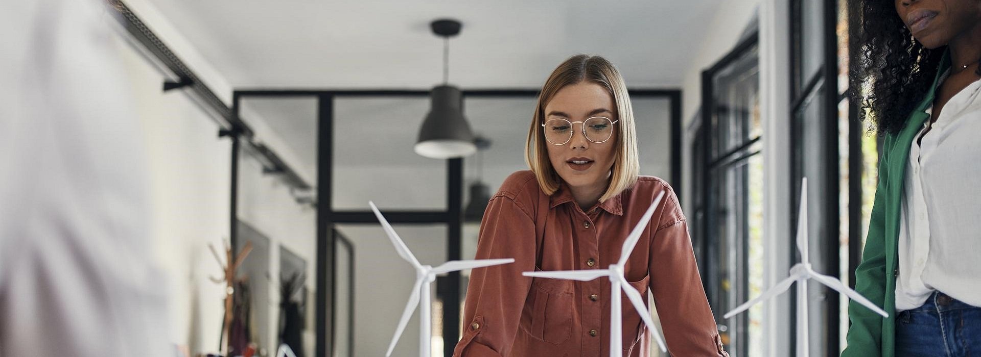 Tre colleghe in sala riunioni osservano dei modellini di pale eoliche