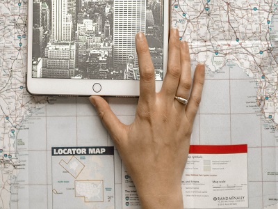 Mano femminile che usa un tablet posato sopra una cartina geografica