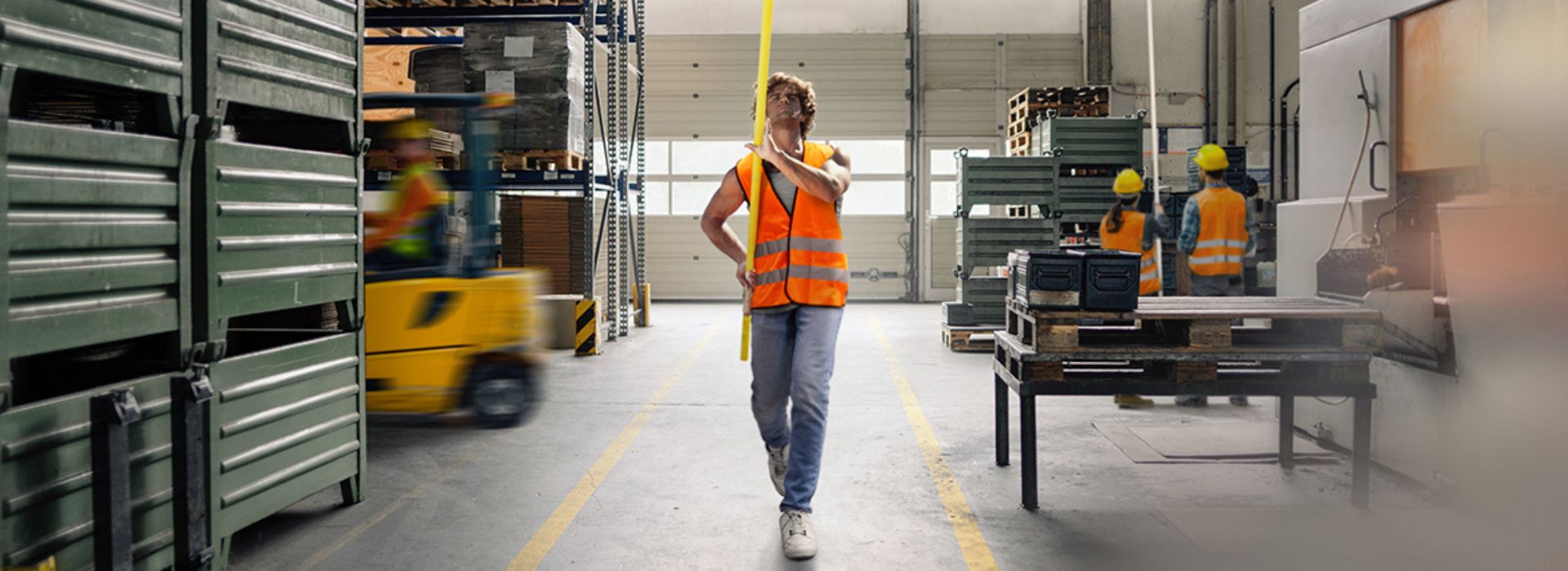 Degli operai lavorano in un magazzino indossando caschi protettivi e gilet arancioni