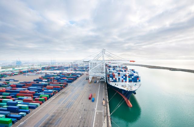 Vista di un porto commerciale con container di merci impilati e una nave attraccata carica di container