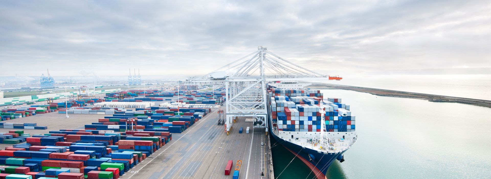 Vista di un porto commerciale con container di merci impilati e una nave attraccata carica di container