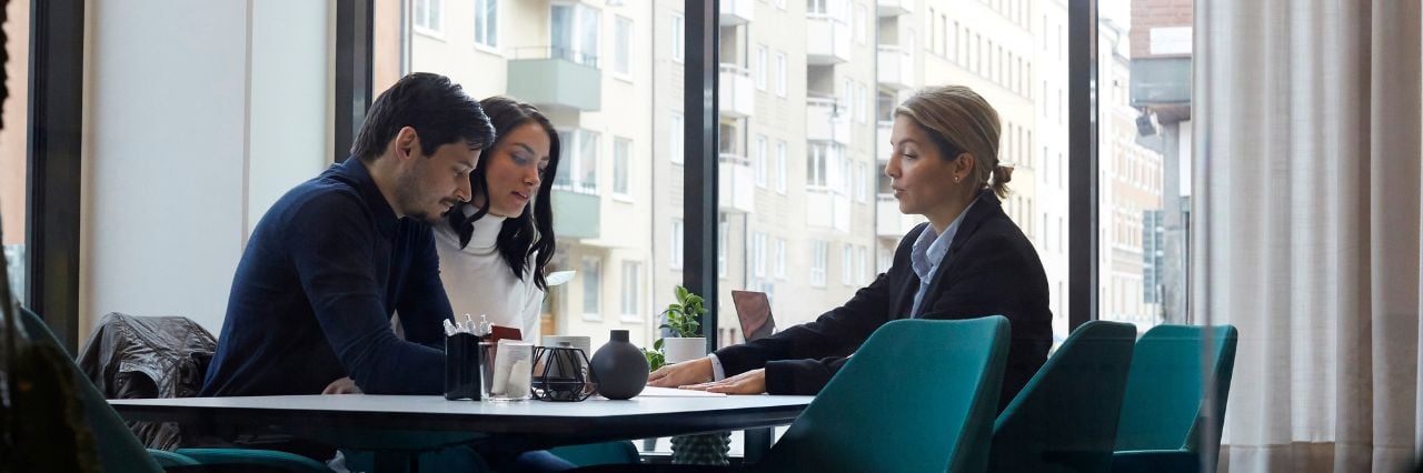 Tre persone sedute a un tavolo che discutono in un ufficio con grandi finestre