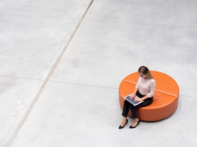 Professionista seduta su un pouf che lavora al computer in ufficio