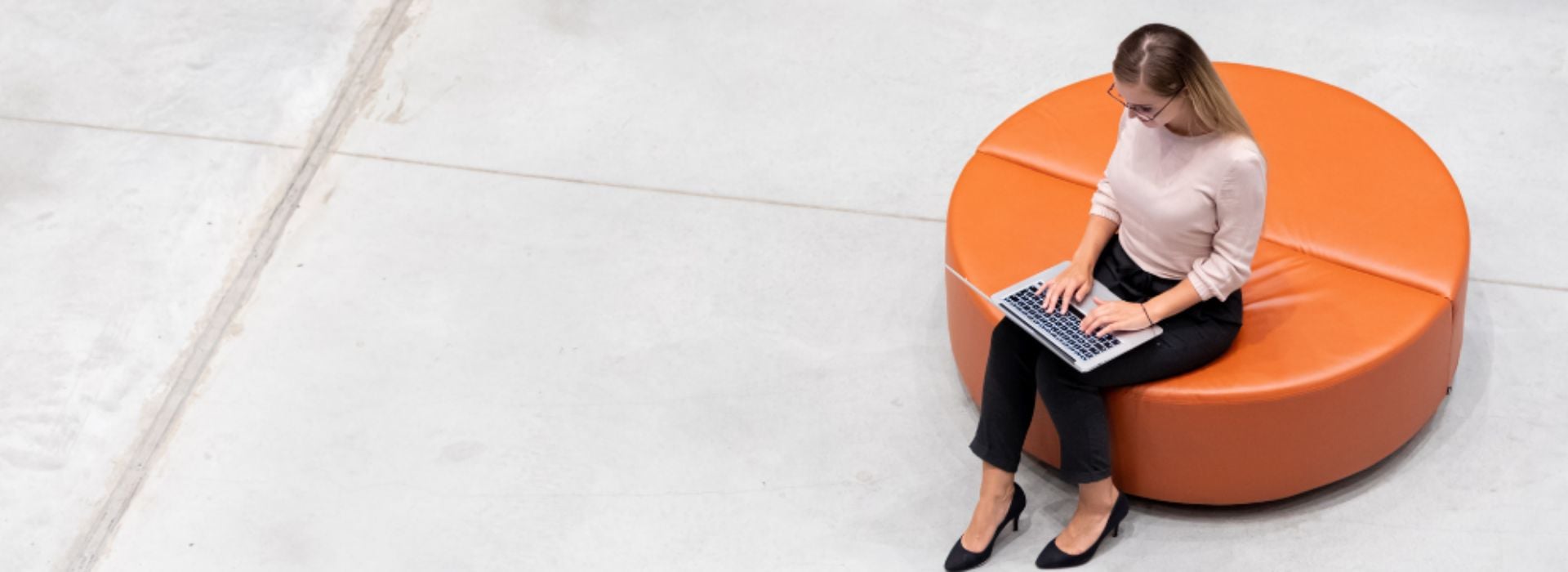 Professionista seduta su un pouf che lavora al computer in ufficio