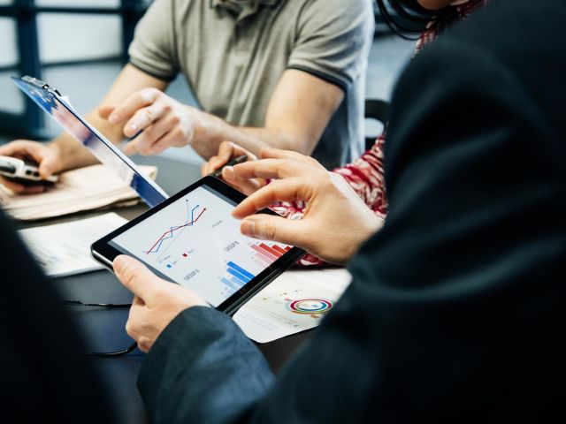Un manager controlla dei dati sul tablet e altri colleghi si confrontano