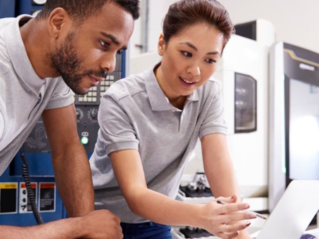 Due colleghi in un'azienda esaminano dei dati sul computer, discutendo le sfide e le opportunità di trasferire la produzione manifatturiera