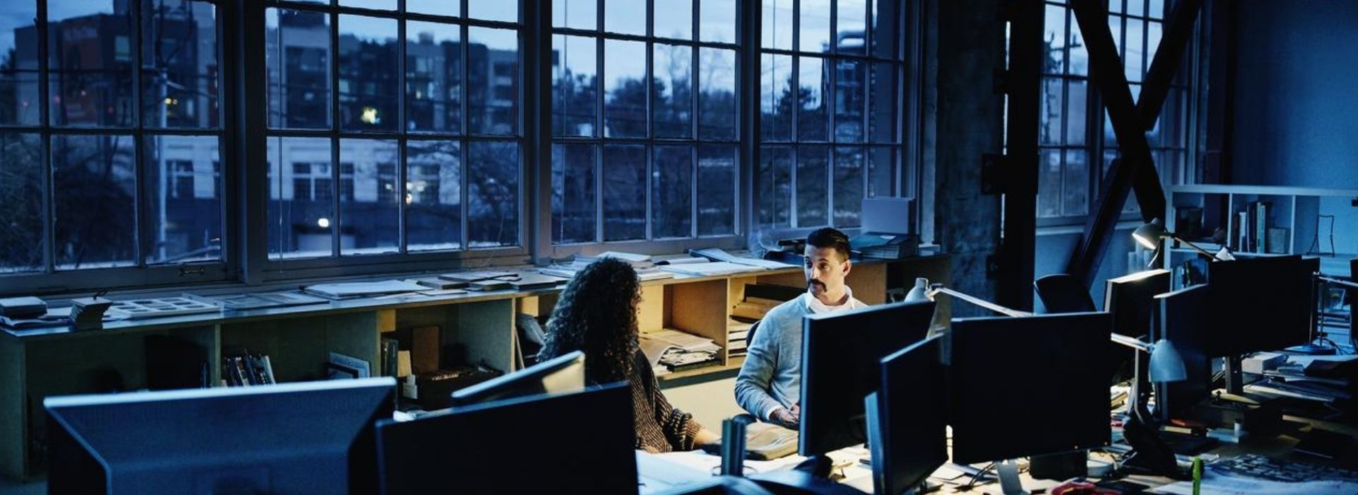 Due colleghi sedute alle loro scrivanie in un ufficio open space si confrontano 