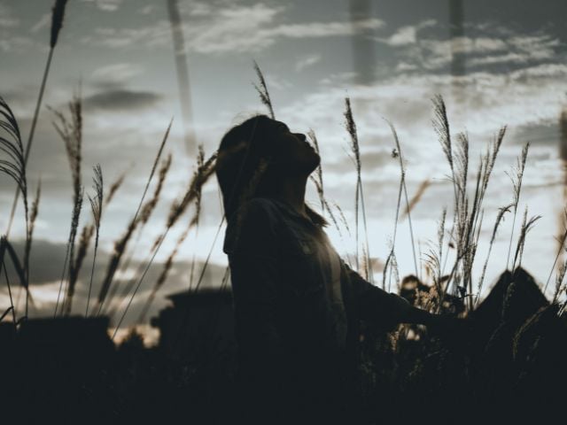 Giovane ragazza in un campo con il viso rivolto verso il cielo nuvoloso.