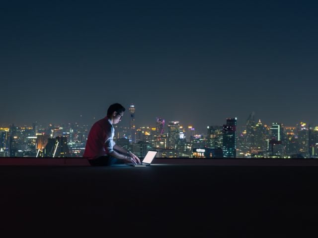 Un imprenditore lavora sul terrazzo di un palazzo, di sera, con vista sulla città illuminata