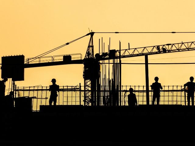 Gru e operai in un cantiere al tramonto