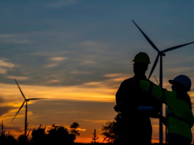 Due tecnici al lavoro in un parco eolico al tramonto