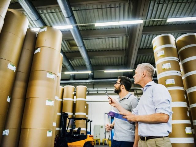 Due lavoratori in un magazzino preparano un ordine di grandi rotoli di carta