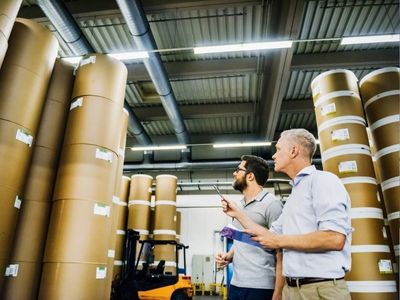 Due lavoratori in un magazzino preparano un ordine di grandi rotoli di carta