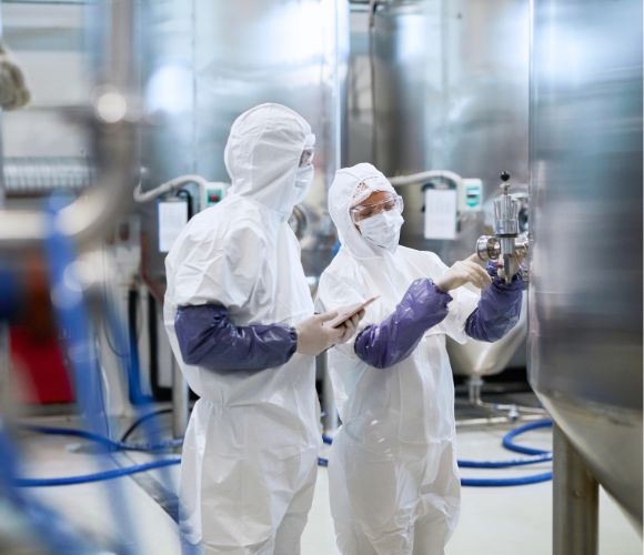 Due ricercatori conducono controlli in un laboratorio farmaceutico, indossando tute, guanti e mascherine di protezione