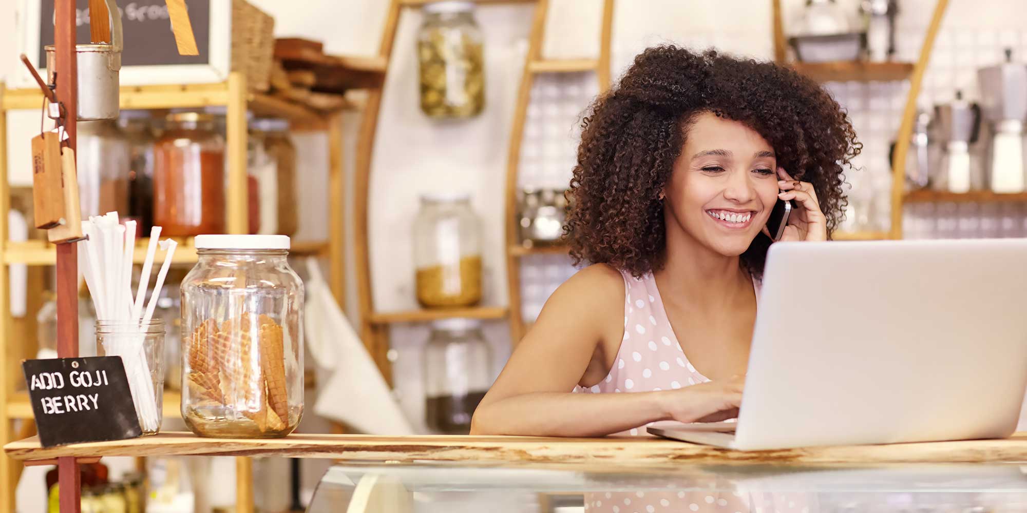 Usmiechnieta kobieta rozmawia przez telefon na przeciw laptopa