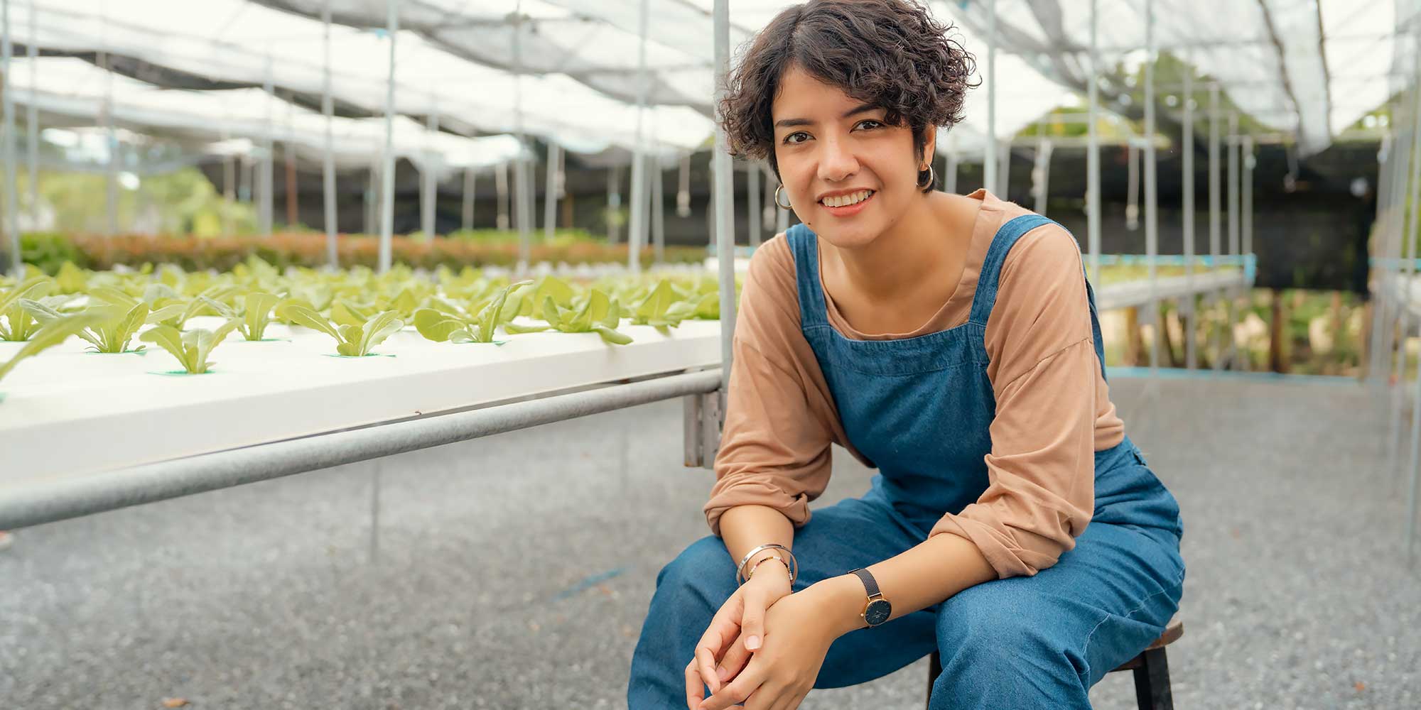 Kobieta siedzi w szklarni pełnej roslin