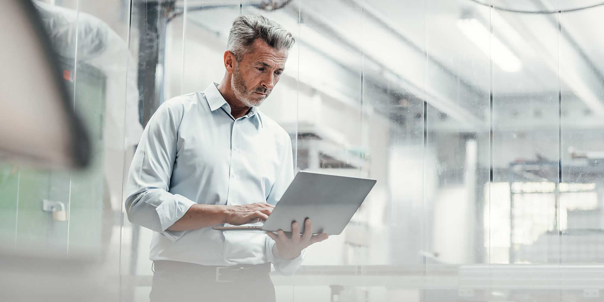 Mężczuzna w białej koszuli stoi i trzyma w rekach laptop