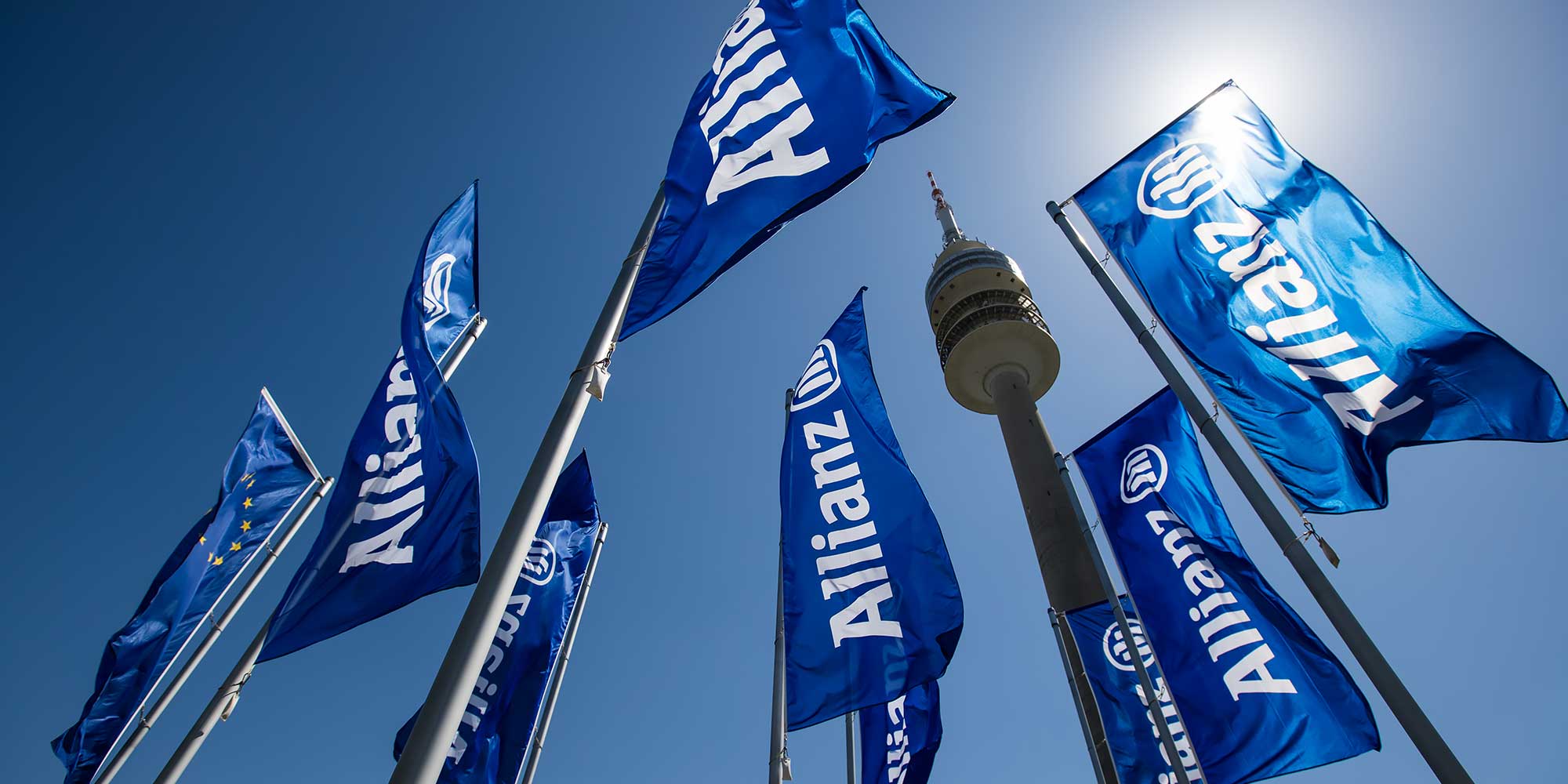 Flagi Allianz Trade na masztach na tle błękitnego nieba