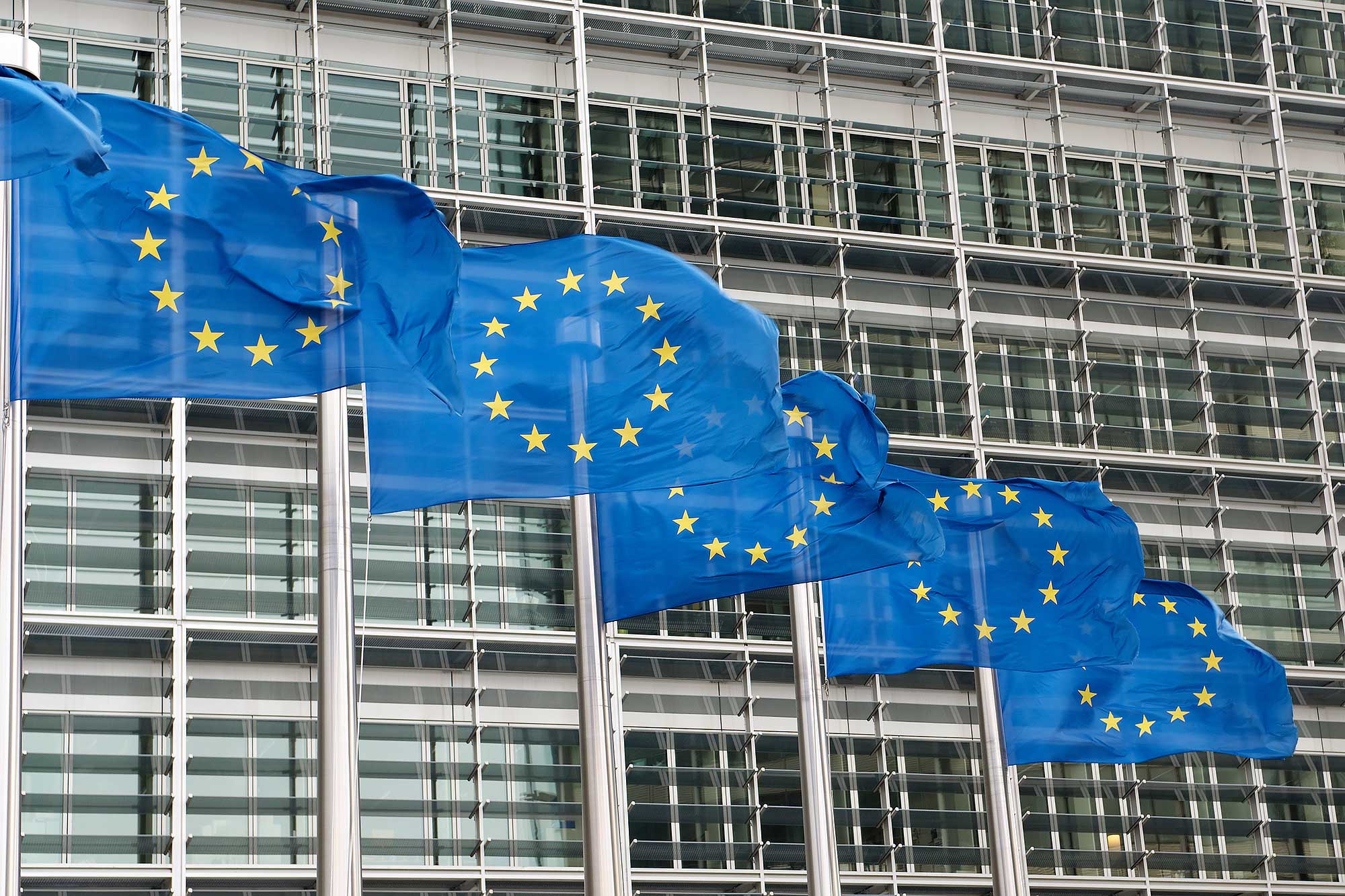 Trzy flagi Unii Europejskiej powiewające na zewnątrz budynku