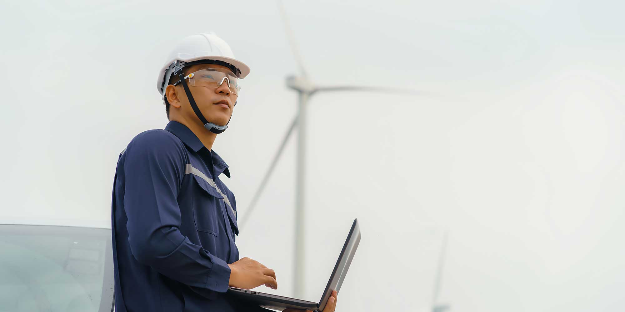 Azjatycki pracownik w kasku ochronnym trzyma laptop