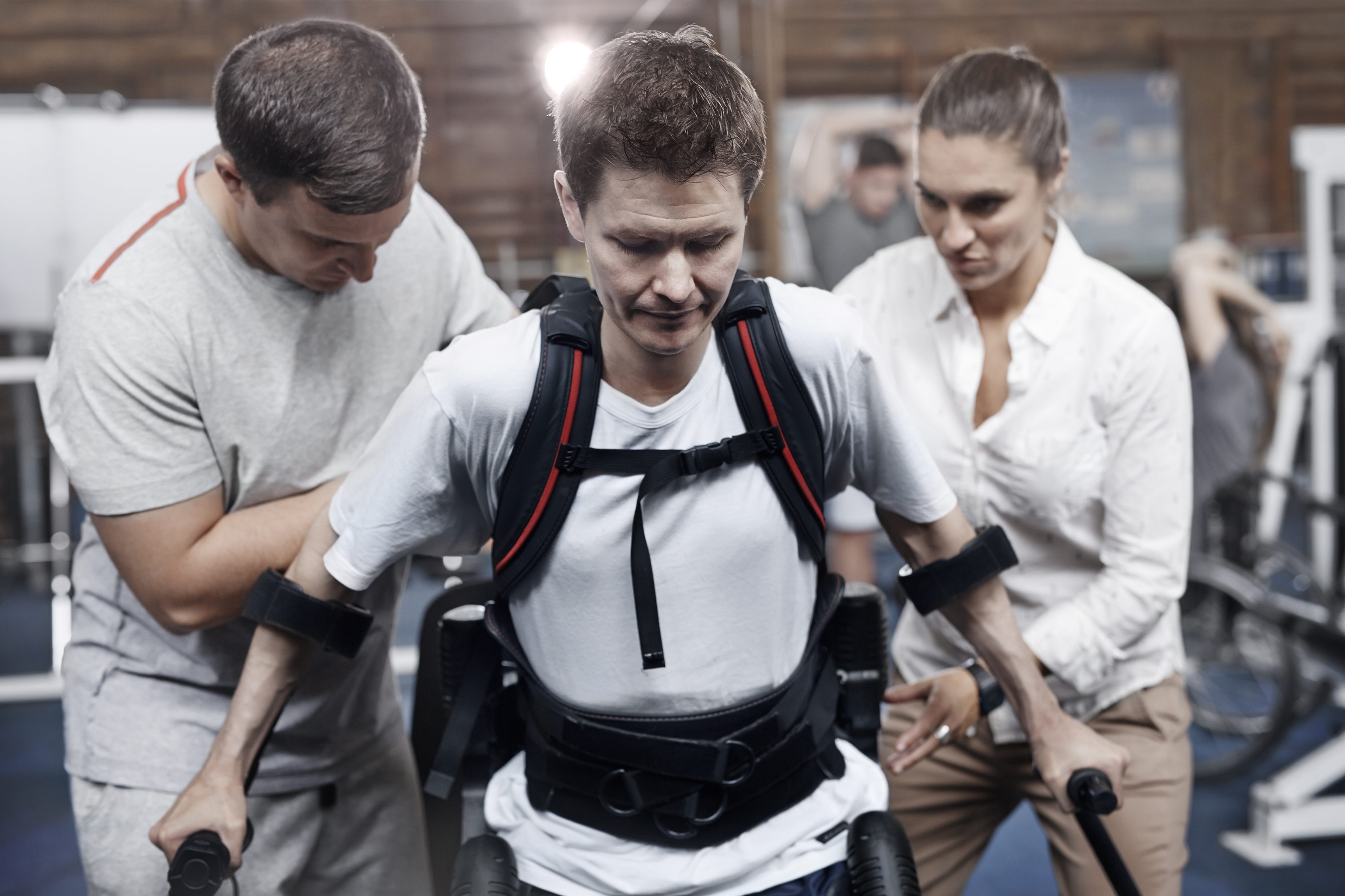 Mężczyzna korzystający z chodzika z pomocą dwóch osób