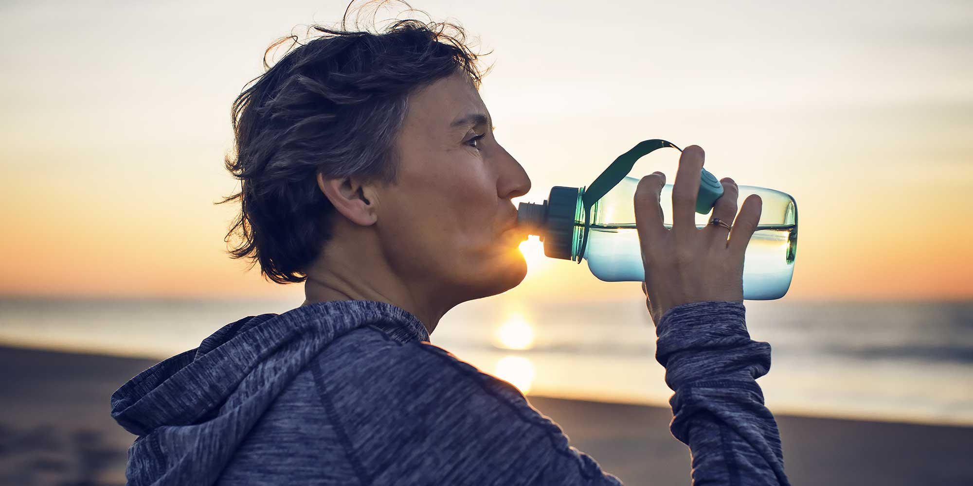 kobieta nad brzegiem morza pije wode z butelki